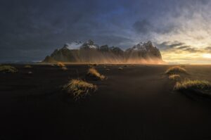 Dramatic mountains emerge from misty coastal sand dunes at sunrise.